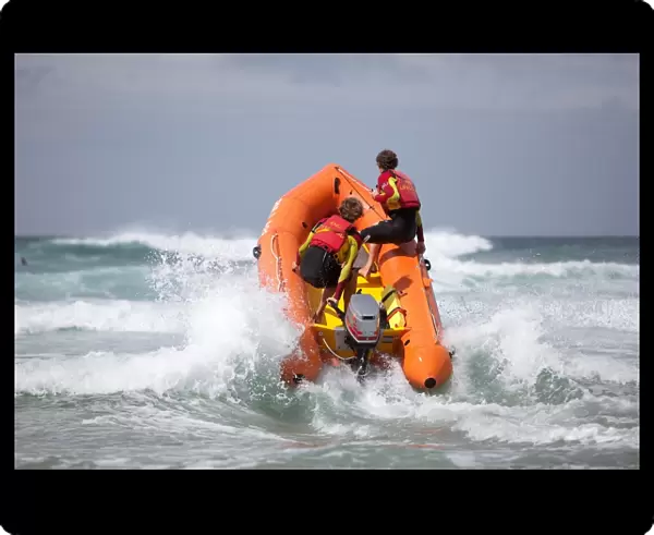 Two RNLI lifeguards heading through a breaking wave on an arancia inshore rescue boat, bow high out of the water