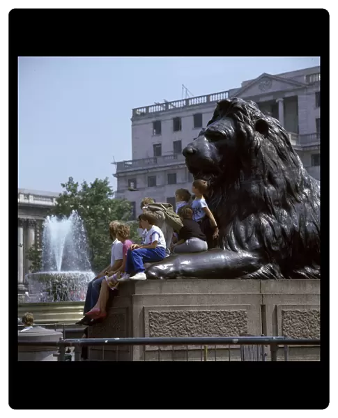 Children and adults sit on a Landseer Lion, Trafalgar Square