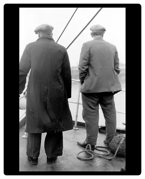 Life on a North Sea trawler - two men on deck in raincoat, jacket, and flat caps, close to shore. Date: 1960s
