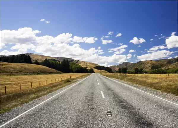 Road - long straight deserted tarmac paved road, rolling hills, white clouds, blue sky. Mackenzie country - New Zealand