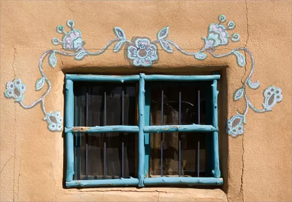 Ornate Window - turquoise painted window mounted in an adobe style building. It is decorated additionally by ornate paintings also in turqoise - Rancho de Taos, New Mexico, USA