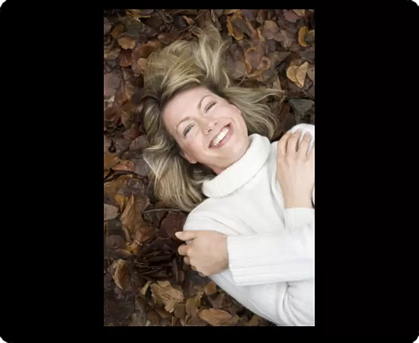 Smiling woman lying on autumn leaves