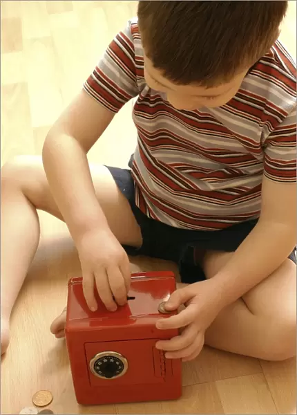 Money box. MODEL RELEASED. Money box. Young boy placing coins into a toy safe
