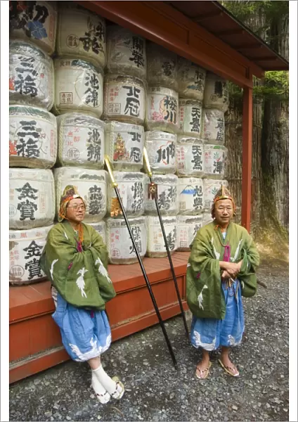 Men traditional clothing sitting in front of colourful sake barrels
