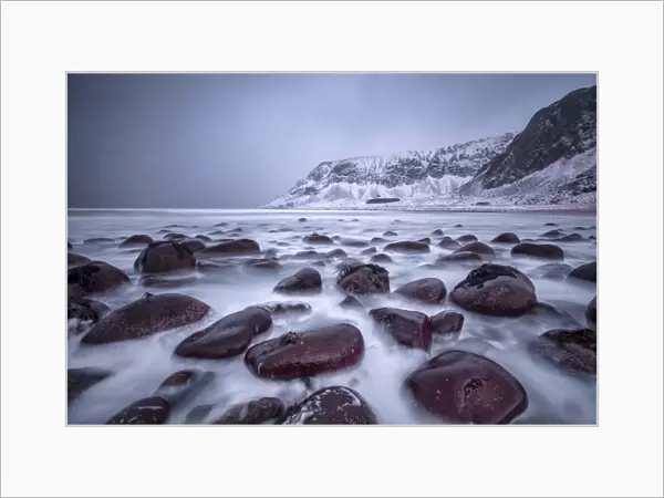 Rocks on the beach modeled by the wind surround the icy sea, Unstad, Lofoten Islands