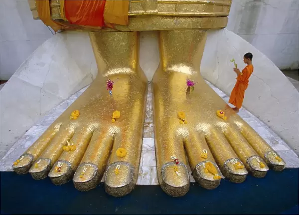 Novice monk praying at the feet of Giant Buddha statue