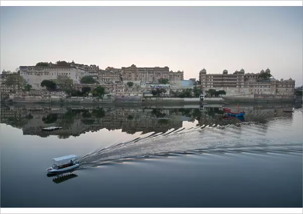 A water taxi passing the City Palace reflected in the still dawn waters of Lake Pichola
