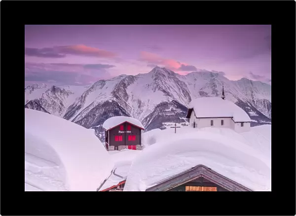 Pink sky at sunset frames the snowy mountain huts and church, Bettmeralp, district of Raron
