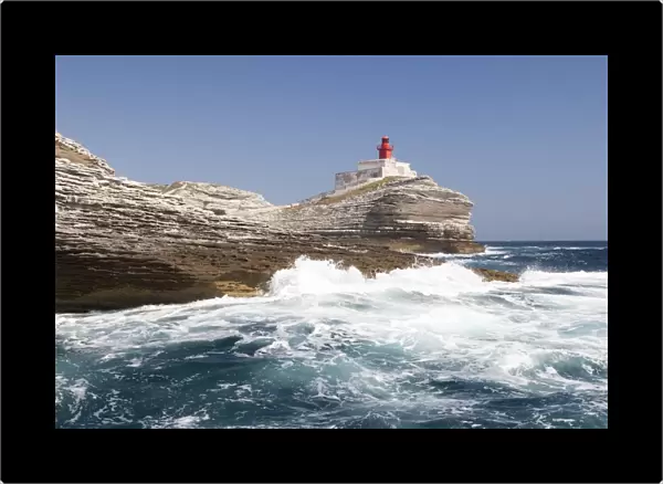 Waves of the turquoise sea crashing on the granite white cliffs and lighthouse, Lavezzi Islands