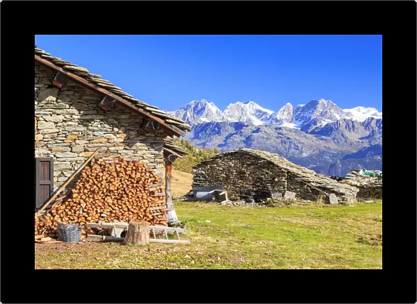 Alpine huts framed by snowy peaks of Bernina Group, Arcoglio Alp, Val Torreggio, Malenco Valley