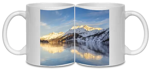 Mountains illuminated by sun at sunset reflected on the icy surfaces of Lake Sils