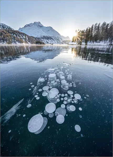 Ice bubbles trapped in frozen Lake Sils at sunset with Piz Da La Margna in background