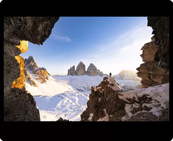 Hiker on rocks admiring Tre Cime di Lavaredo and Monte Paterno covered with snow at