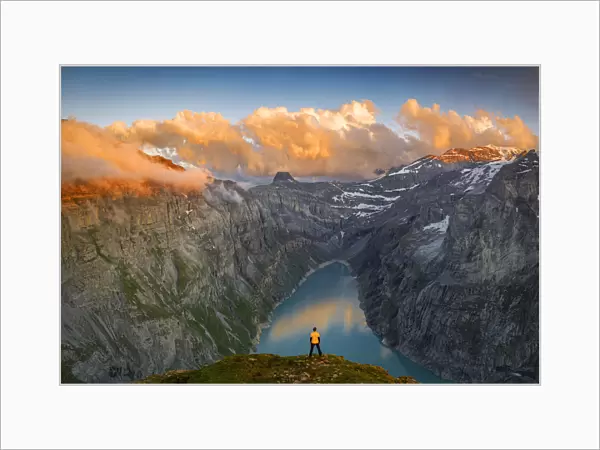 Man standing on rocks looking at clouds at sunset over lake Limmernsee, aerial view