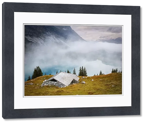 Hut on mountain ridge above lake Oeschinensee covered by mist, Bernese Oberland