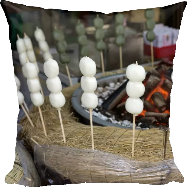 Japanese snack called dango (three sticky rice cake balls on a skewer) warming beside hot coals