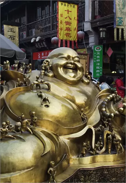 A golden statue of a reclining laughing Buddha covered in small Buddhas