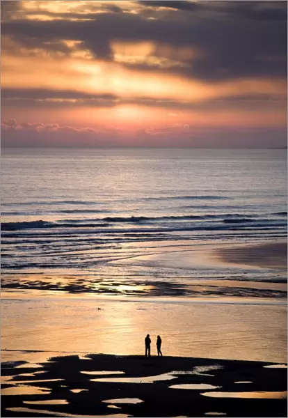 Man and woman in silhouette looking out over North Sea at sunsrise from Alnmouth Beach