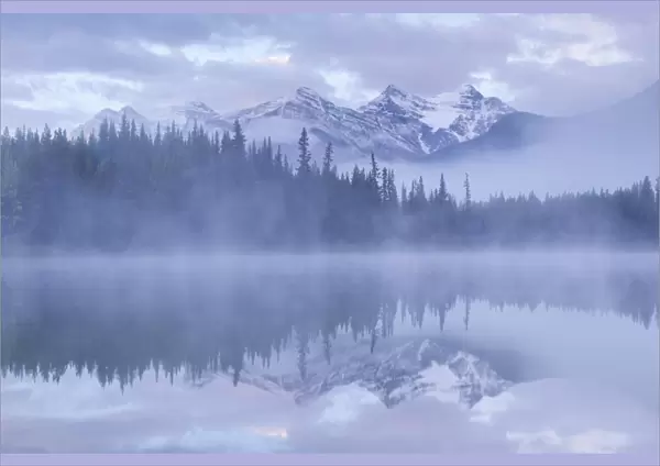 Snow capped mountains reflect in a misty Herbert Lake, Canadian Rockies, Banff National Park