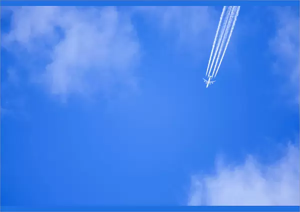 An airplane flies across a blue sky leaving vapour trails
