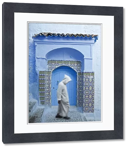 Man in Burnoose walking past blue doorway, Chefchaouen, Morocco