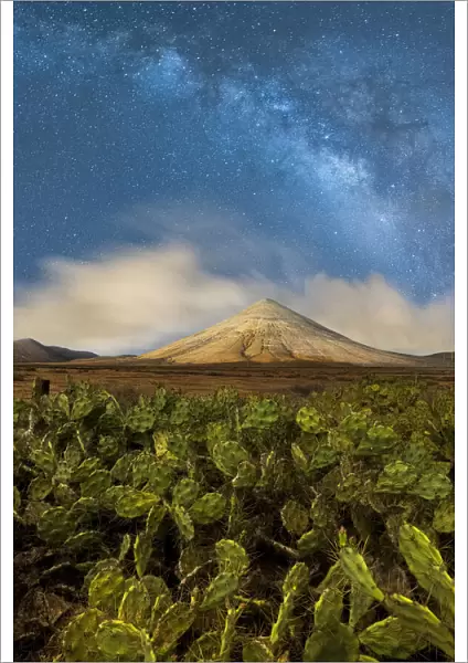 Milky Way glowing over Montana del Fronton peak and cactus plants, La Oliva