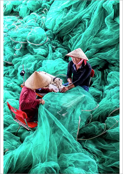 Vietnam, Cam Ranh, two men repair green fishing nets using a sewing machine