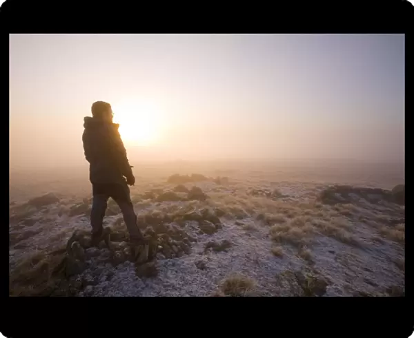 A walker on the summit of Caudale Moor at sunset in the Lake District UK