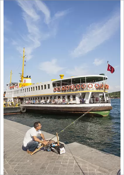 Turkey, Istanbul, Man fishing on quayside, and passenger ferry in Karakoy Cruise Terminal, Bosphorus Strait
