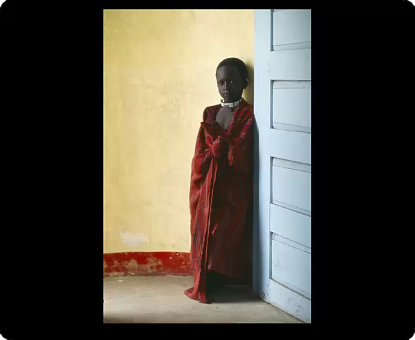 20053695. TANZANIA Ngorongoro Masai child standing between yellow wall and blue door