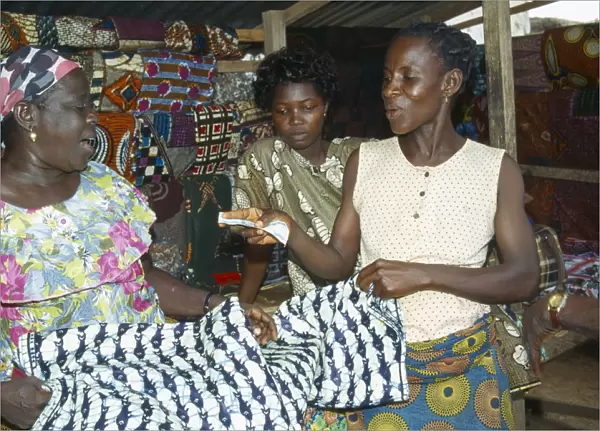 20061108. GHANA West Markets Woman purchasing length of batik dyed cloth with fish design
