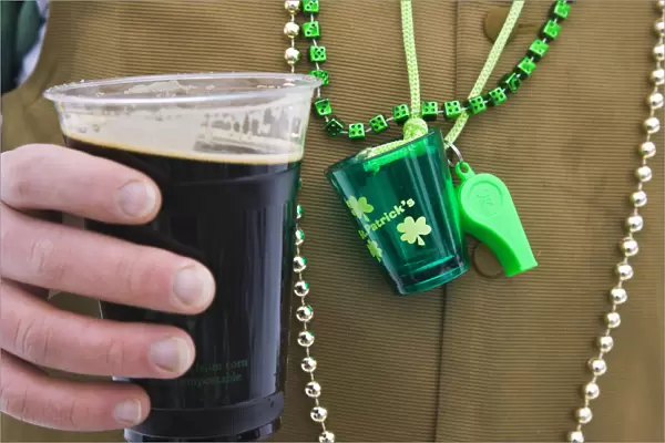Detail of man wearing various green items whilst drinking pint of stout beer