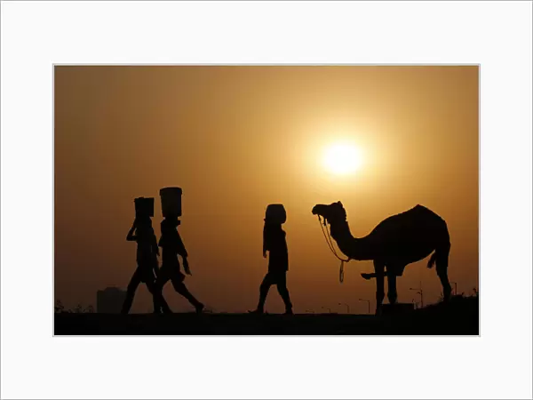 Girls carrying buckets filled with water are silhouetted against the setting sun as