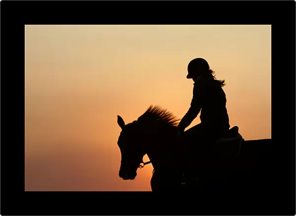 A horsewoman is silhouetted as she trains her horse during a ride at sunset at a riding