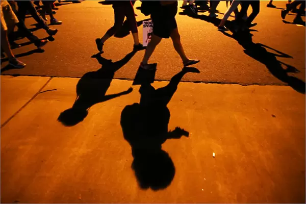 Protesters shadows mark the sidewalk as they march during another night of protests
