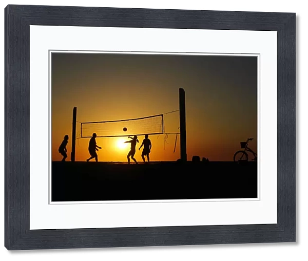 Beachgoers play volleyball at the beach as the sun sets in Carlsbad, California