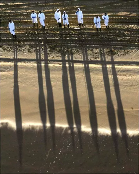WORKERS CAST SHADOWS ON A CLEAN BEACH IN THE SPANISH NORTHERN COAST