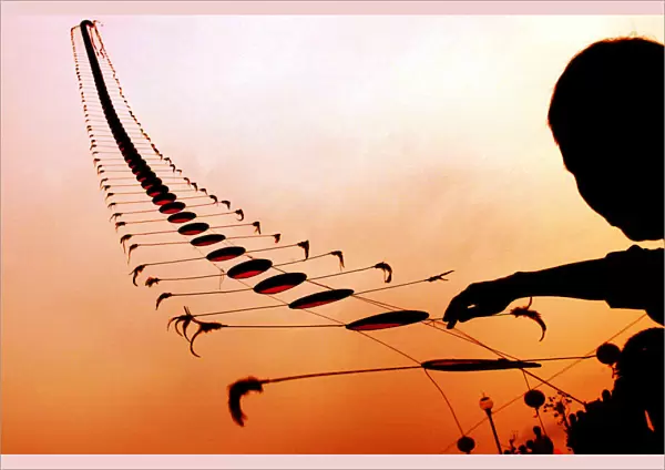 AN ELDERLY CHINESE MAN FLIES A KITE IN THE SHAPE OF A CENTIPEDE AT SUNSET IN WUHAN