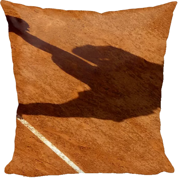 THE SHADOW OF A TENNIS PLAYER AS HE SERVES IS CAST ON THE CLAY