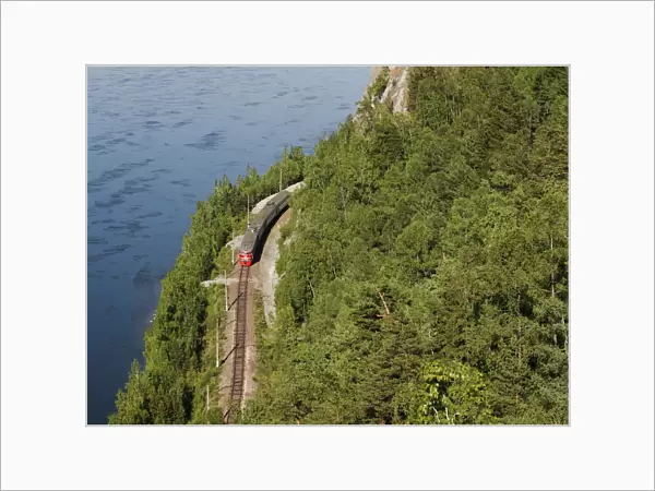 A passenger train moves along a railway along the bank of the Yenisei River near the