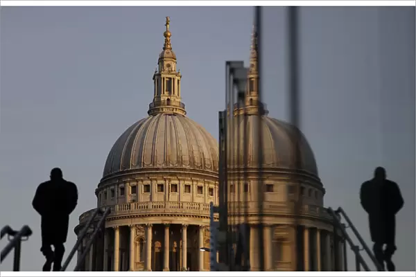 A pedestrian is reflected in glass as he walks towards St Pauls Cathedral in the