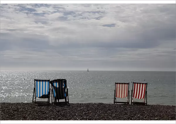 A woman sunbathes in a deckchair by the sea on a sunny day on Brighton Beach in southern