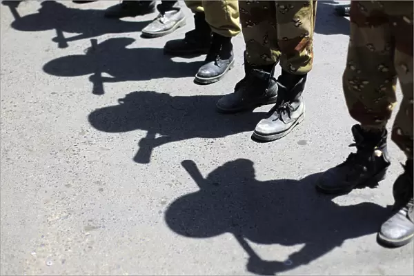 Shadows of army soldiers holding batons are cast on the ground as they stand in line to