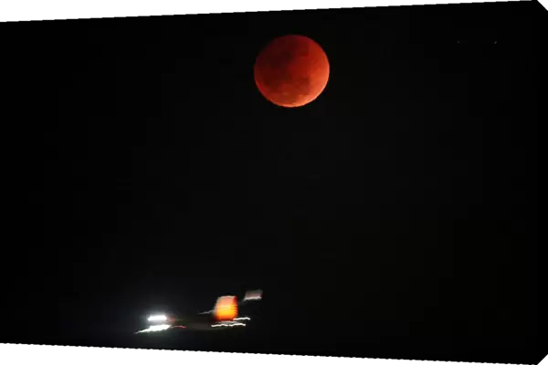 A lunar eclipse of a full Blue Moon is seen as an airplane passes by in Ahmedabad