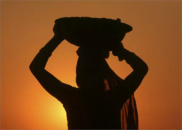 A woman labourer carrying cement is silhouetted against the setting sun at the site of a
