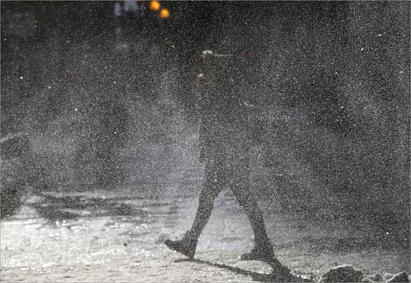 A woman walks through a gust of blowing snow in frigid cold temperatures though downtown