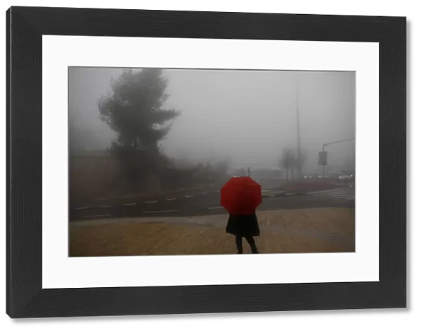 A woman holds an umbrella as she stands on the sidewalk during a foggy day in Jerusalem