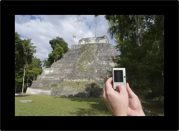 Tourist using a digital camera to photograph a Mayan temple at Yaxha nr Tikal Guatemala