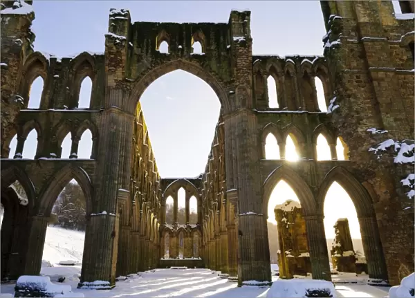 Sunlight shining through arched windows of ruined cistercian abbey in snow, Rievaulx Abbey, North York Moors N. P