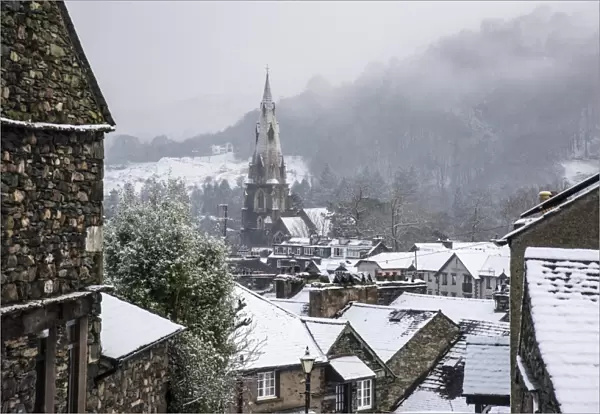 View across snow covered rooftops towards church spire in town, St. Marys Church, Ambleside, Lake District N. P